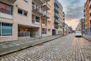 Una strada acciottolata fiancheggiata da edifici residenziali a più piani, con balconi e ampie finestre.