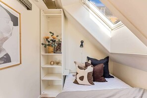 Una camera da letto con un lucernario, un letto con cuscini, uno scaffale con oggetti decorativi e un quadro appeso al muro.