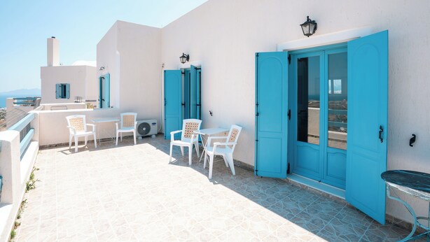Una terrazza sul tetto con sedie bianche, un tavolo e porte blu.