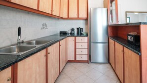 Cucina con mobili in legno, frigorifero in acciaio inox, lavello a due vasche e un piano di lavoro con macchina da caffè.