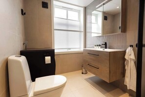 Et moderne badeværelse med toilet, håndvask, underskab og et vindue.