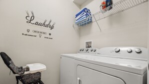 A laundry area with a washing machine, a drying rack, and a chair with a laundry bag. - EV_1800 - 6BR / 5BA Luxury Villa w/ Private Pool & Spa, Game Room, Resort Access (Kissimee)