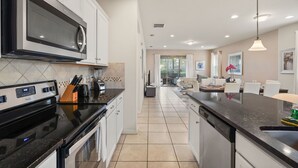A modern kitchen with a built-in microwave, stove, and dishwasher. There is a dining area with a table and chairs visible through an open doorway. - EV_1800 - 6BR / 5BA Luxury Villa w/ Private Pool & Spa, Game Room, Resort Access (Kissimee)