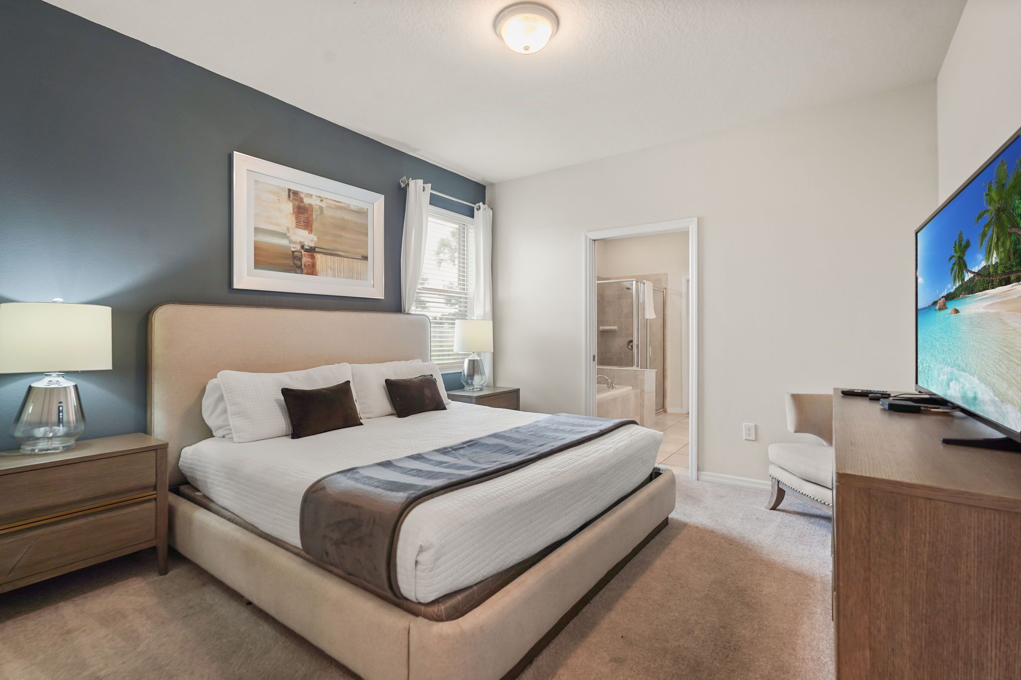 A hotel room with a bed, a television, a desk, and a bathroom visible through an open door.