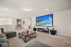 A living room with a large flat-screen TV, a sofa, a coffee table, and a TV stand with decorative items. - EV_1800 - 6BR / 5BA Luxury Villa w/ Private Pool & Spa, Game Room, Resort Access (Kissimee)