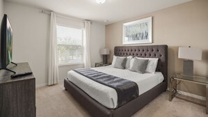 A bedroom with a large bed, bedside lamps, a TV on a wooden stand, and a window with curtains. - EV_1800 - 6BR / 5BA Luxury Villa w/ Private Pool & Spa, Game Room, Resort Access (Kissimee)