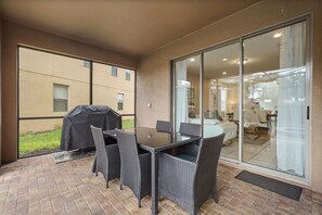 Une terrasse avec une table et des chaises, un barbecue et une porte-fenêtre coulissante donnant accès à un espace intérieur.