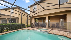 A swimming pool with a glass enclosure, a covered seating area, and a building with a beige exterior. - EV_1800 - 6BR / 5BA Luxury Villa w/ Private Pool & Spa, Game Room, Resort Access (Kissimee)