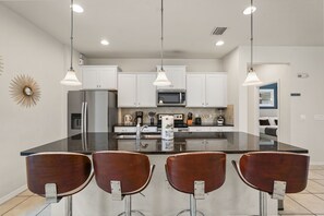 A modern kitchen with white cabinets, a central island with bar stools, and pendant lighting. - EV_1800 - 6BR / 5BA Luxury Villa w/ Private Pool & Spa, Game Room, Resort Access (Kissimee)