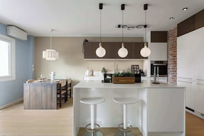 Une cuisine moderne dotée d’un îlot central, de tabourets de bar, de luminaires suspendus et d’un mur d’accent en briques.