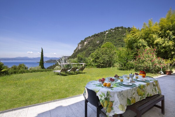 An outdoor dining area with a table set for breakfast, overlooking a scenic view of a lake and mountains. - Apartment Agave with Lake View (Bardolino)