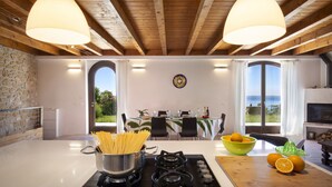 Een keuken met een fornuis, een pan pasta, een schaal sinaasappels en een eethoek met een tafel en stoelen.