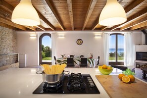A kitchen with a stove, a pot of pasta, a bowl of oranges, and a dining area with a table and chairs. - Apartment Agave with Lake View (Bardolino)