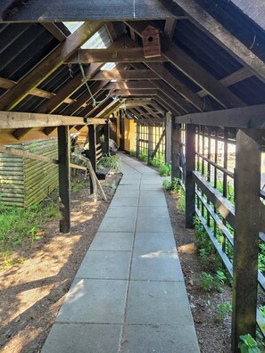 A covered walkway with wooden beams, a concrete path, and a wooden fence on one side. - Historic house from 1877 in Thy National Park (Stenbjerg)