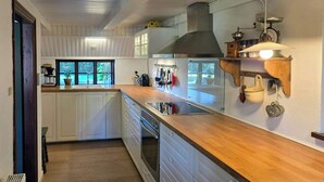 Cocina con armarios blancos, encimera de madera, extractor de acero inoxidable y ventana con vistas al verdor.