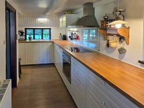 A kitchen with white cabinets, a wooden countertop, a stainless steel range hood, and a window with a view of greenery. - Historic house from 1877 in Thy National Park (Stenbjerg)