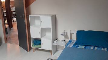 A bedroom with a bed, a white wardrobe, a desk with a lamp, and a door leading to a bathroom.