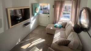 A living room with a sofa, ottoman, TV, and a window with curtains.
