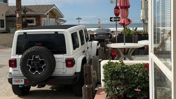A white SUV parked outside a building with a stop sign and a one-way sign.