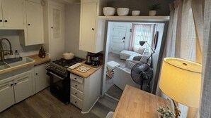 A compact kitchen with a stove, sink, and cabinets, leading to a small dining area with a table and a fan.