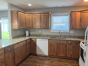 A kitchen with wooden cabinets, a granite countertop, a dishwasher, and a window with blinds. - Peaceful 3 bedroom handicapped accessible house with AC in charming Hamilton. (Hamilton)