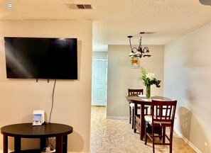 A dining area with a round table, chairs, a vase with flowers, a wall-mounted TV, and a ceiling fan. - Your Getaway Awaits (Pensacola)