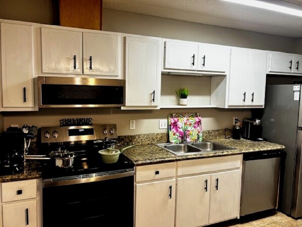 A kitchen with white cabinets, a stainless steel stove, a sink, and a refrigerator. - Your Getaway Awaits (Pensacola)