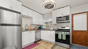 A modern kitchen with white cabinets, stainless steel appliances, a built-in microwave, and a wooden door. - Cozy Pacific Beach 2BR Patio Fire Pit (San Diego)