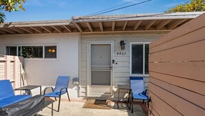 A small house with a screened door, numbered 4467, and a porch with two blue chairs and a table. - Cozy Pacific Beach 2BR Patio Fire Pit (San Diego)