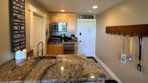 A kitchen with granite countertops, wooden cabinets, a stainless steel refrigerator, and a sign indicating 'Ski Tips Up'. - Ski-in, Chill-out Tahoe Donner Condo (Truckee)