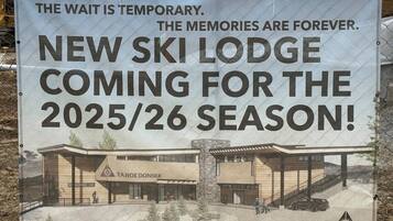 Une banderole fait la publicité d’un nouveau chalet de ski doté d’une architecture moderne, avec une entrée imposante et un espace abrité pour les véhicules.