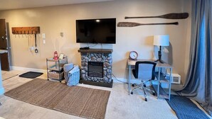 A living room with a stone fireplace, a flat-screen TV, a desk with a lamp, and a large paddle on the wall. - Ski-in, Chill-out Tahoe Donner Condo (Truckee)