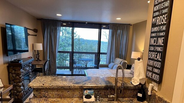 A kitchen with granite countertops, a stainless steel sink, a dining area with a table and chairs, and a large window with curtains. - Ski-in, Chill-out Tahoe Donner Condo (Truckee)