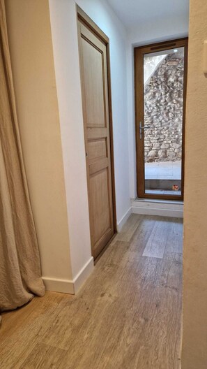 A hallway with a wooden door, a stone wall outside, and a wooden floor. - Charming village house in Provence with courtyard (CHATEAUNEUF DE GADAGNE)