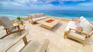 Une terrasse avec un canapé, des chaises et un foyer extérieur, le tout offrant une vue sur l’océan.