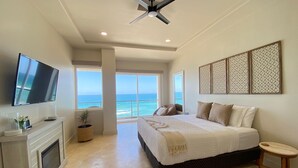 Une chambre à coucher avec un lit, une télévision, un ventilateur de plafond, une cheminée et une vue sur l’océan.