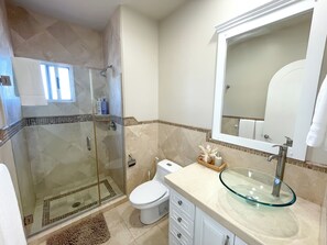 A bathroom with a glass-enclosed shower, a toilet, a sink with a glass basin, and a mirror above the sink. - Beachfront Penthouse with Large Private Rooftop Patio with Wood Burning Firepit (Playas de Rosarito)