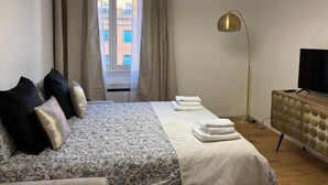 Ein Hotelzimmer mit einem Bett, einem Fernseher, einer Stehlampe und Blick auf Gebäude.
