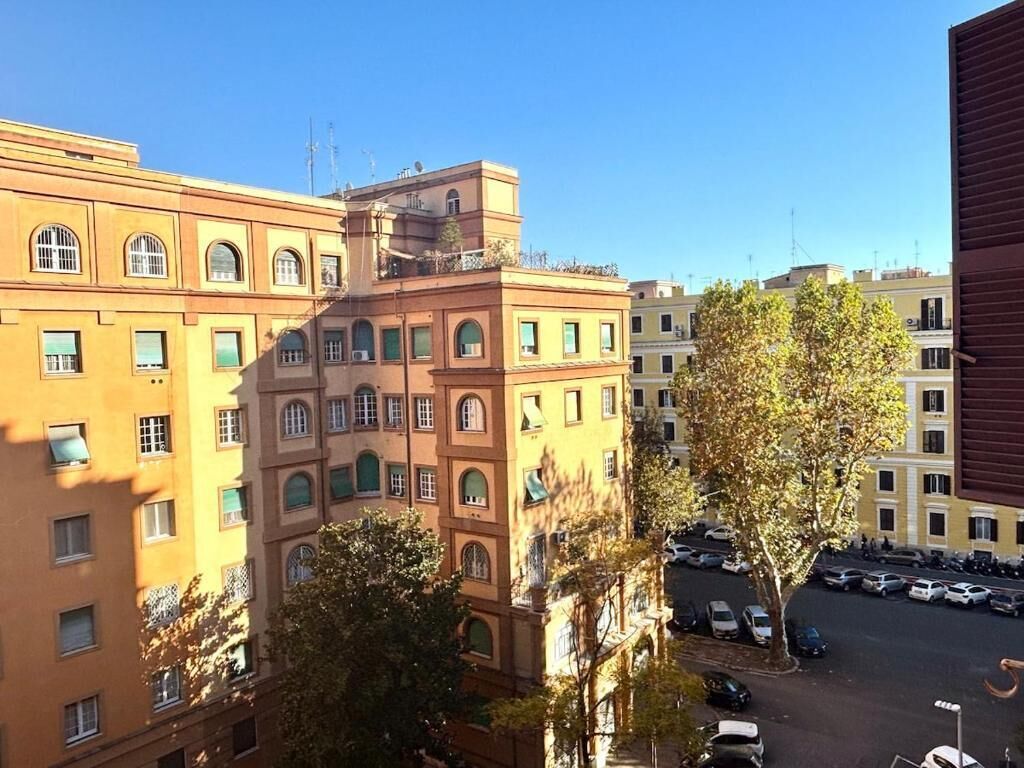 Un edificio a più piani con un cortile interno, auto parcheggiate e alberi.