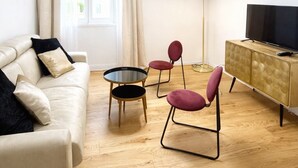 Ein modernes Wohnzimmer mit Sofa, zwei Sesseln, einem kleinen Tisch, einer Stehlampe, einem Fernseher und einem Schrank.