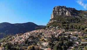 A town with buildings on a hillside, a prominent rocky cliff, and mountains in the background.