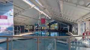 Una piscina interior con techos altos, vigas estructurales visibles y una vista despejada del área de la piscina.