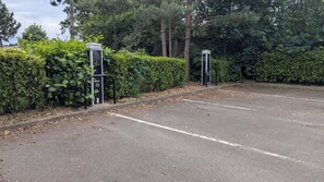 Pysäköintialue, jossa on kaksi sähköautojen latauspistettä, ja jonka ympärillä on tiheää kasvillisuutta ja puita.