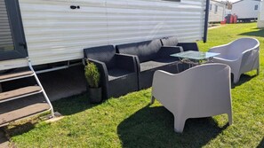 Una caravana con un patio amueblado que incluye un conjunto de sofás, una mesa de vidrio y dos sillas.