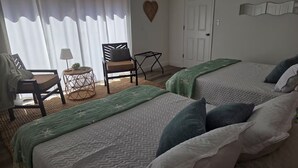 A bedroom with two beds, a chair, a small table, and a heart-shaped decoration on the wall. - Hibiscus House - Relaxing Tropical Getaway with Pool (Fort Myers)