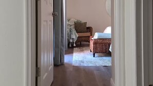 A hallway leading to a bedroom with a bed, a chair, and a small table. - Hibiscus House - Relaxing Tropical Getaway with Pool (Fort Myers)