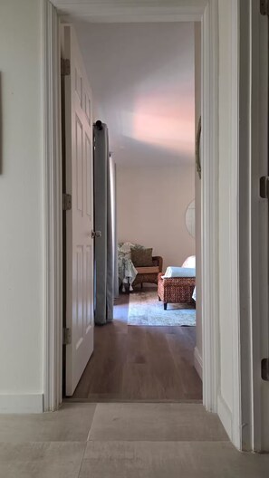 Ein Flur, der zu einem Schlafzimmer führt, mit einem Bett, einem Sessel und einem kleinen Tisch.