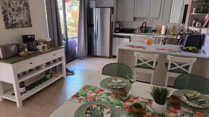 A compact kitchen with a refrigerator, a dining table with chairs, and a small island with a sink. - Hibiscus House - Relaxing Tropical Getaway with Pool (Fort Myers)