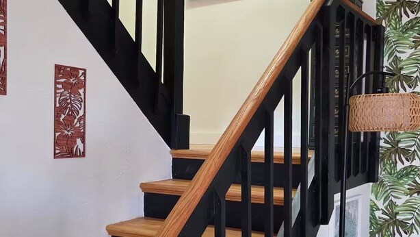 A staircase with wooden steps and black railings, surrounded by wall art and potted plants. - Hibiscus House - Relaxing Tropical Getaway with Pool (Fort Myers)