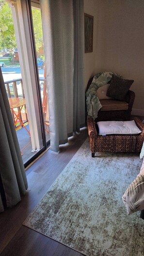 Ein Zimmer mit einem Korbssofa, einem gemusterten Teppich und Blick durch eine Glastür.